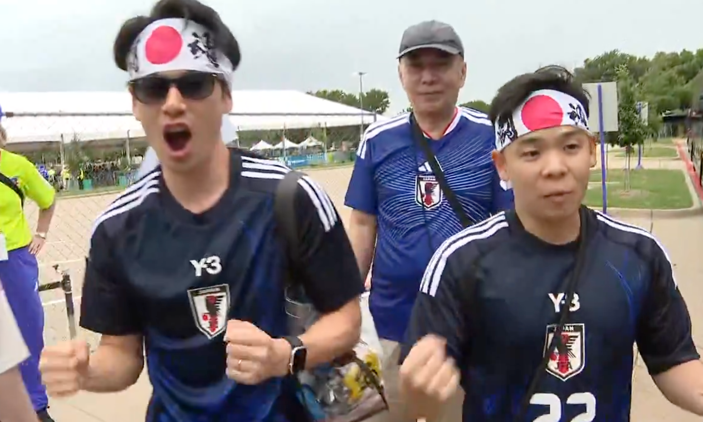 Three radical wearing Japan shot shirts and headbands with reddish circles cheer energetically outdoors