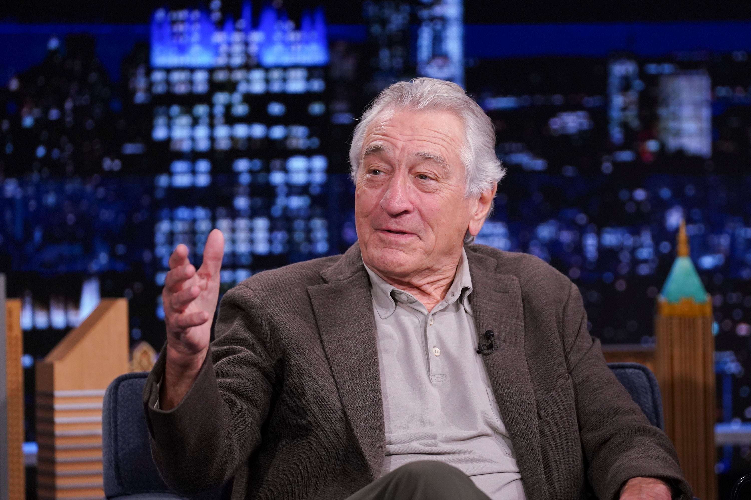 A antheral successful a blazer and garment speaks animatedly during a tv speech amusement against a nighttime cityscape backdrop