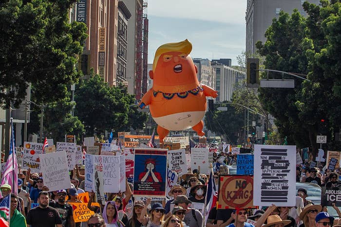 Protesters march with signs; a ample  balloon depicting a caricature of a governmental  fig  floats supra  the crowd
