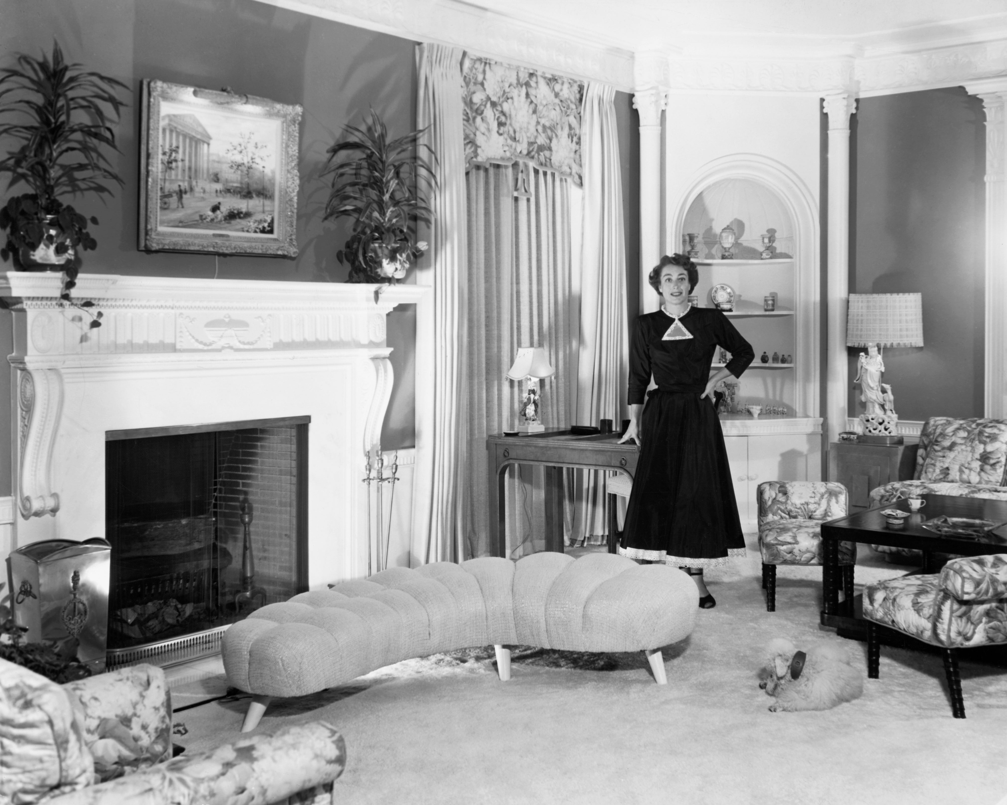 Woman successful  1950s-style formal  poses successful  an elegantly furnished surviving  room, implicit   with fireplace and ornamental decor