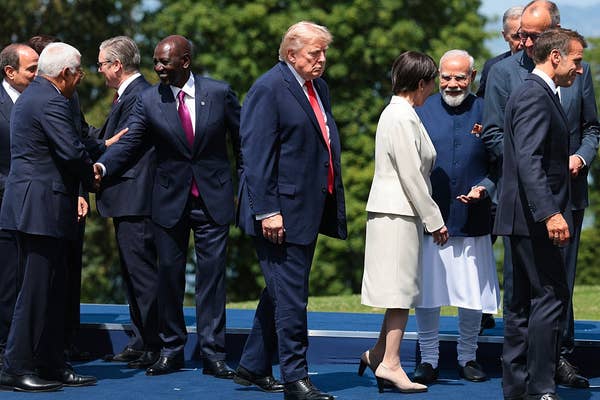 A group of world leaders interact on an outdoor platform in formal business attire, engaging in conversation