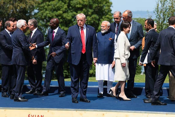 World leaders gathered outdoors on a platform, engaging in conversation and handshakes during a summit
