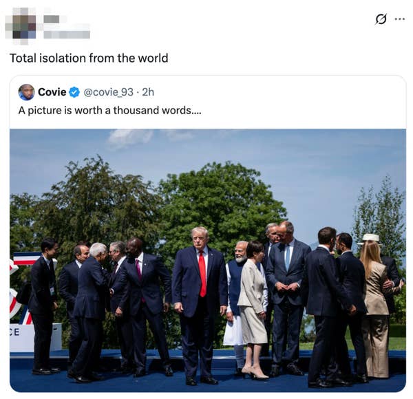 Group of world leaders gathered outdoors, mostly interacting, with one leader standing slightly apart. Trees visible in the background