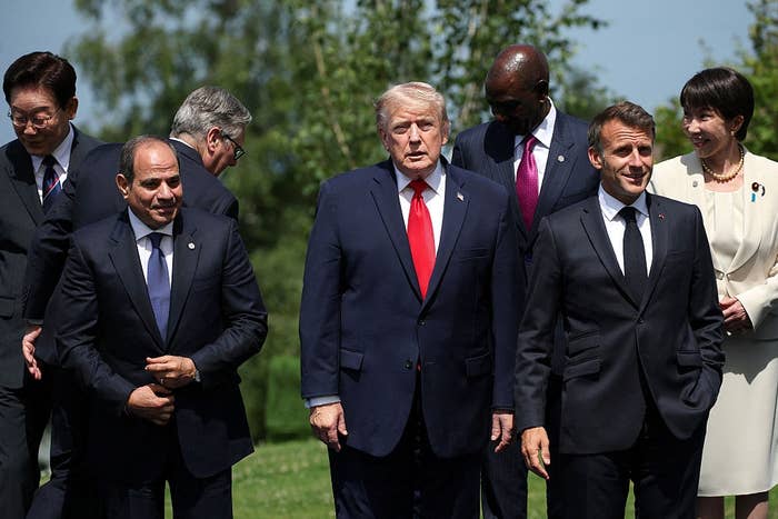 A group of world leaders stands together outdoors, dressed in formal suits and ties, engaged in conversation