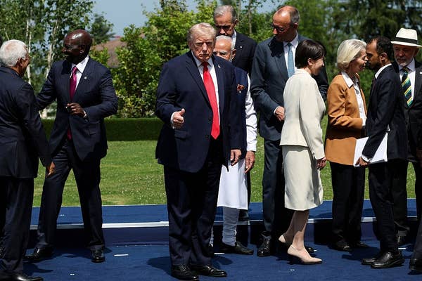 A group of leaders stand and converse outdoors on a platform. One man in a suit gives a thumbs-up to the camera