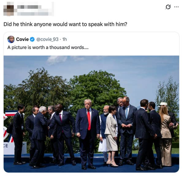 Group of well-dressed leaders stand outdoors, some engaged in conversation. Center figure, in a suit and red tie, looks forward, slightly apart