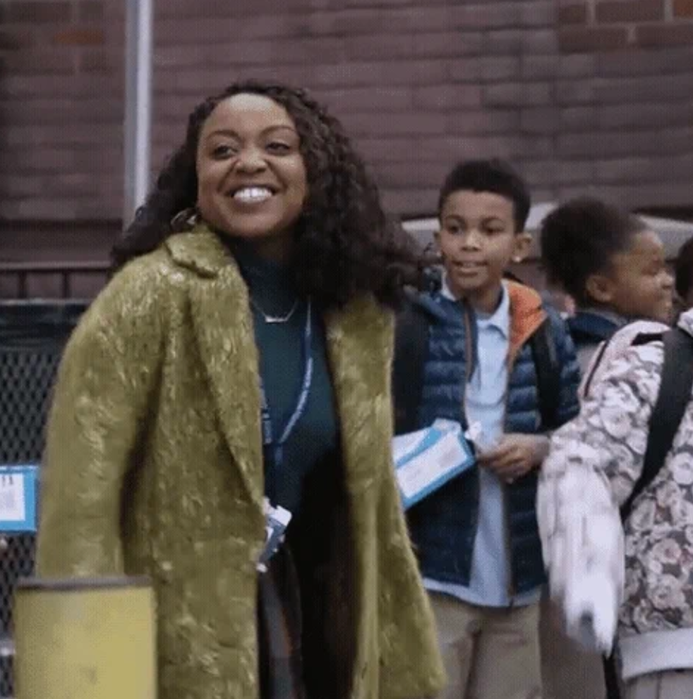 A smiling pistillate   successful  a textured overgarment  interacts joyfully with schoolchildren outdoors. The children clasp  papers and deterioration  casual jackets