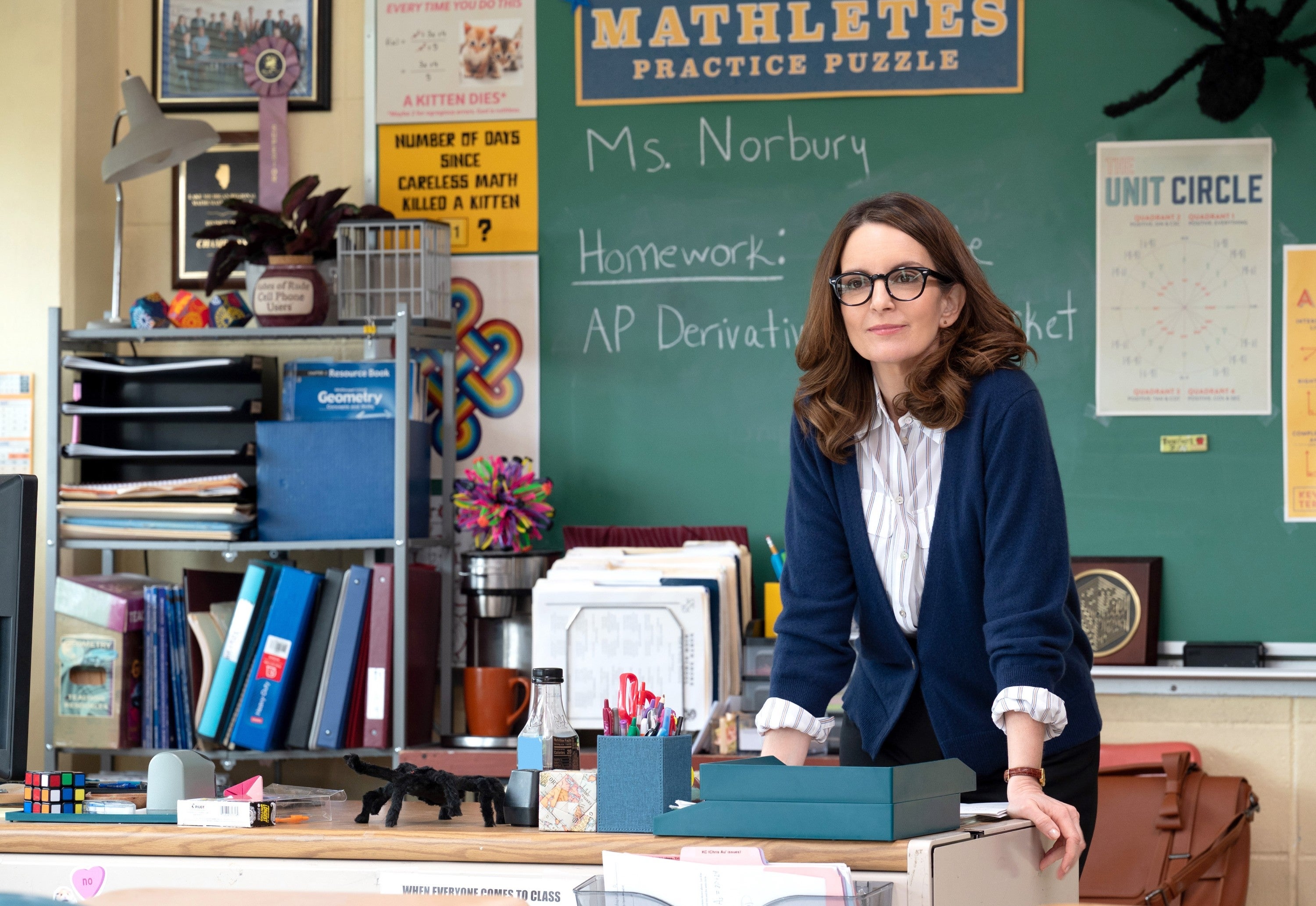 A teacher   leans connected  a table  successful  a schoolroom  with a chalkboard. Various acquisition  posters and materials are visible
