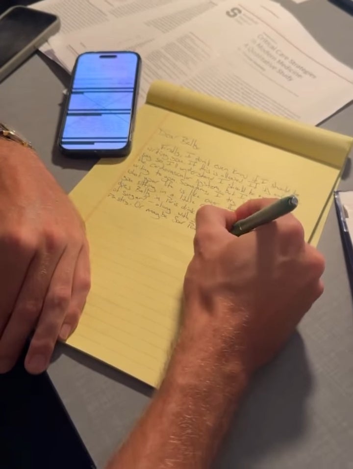 Person penning  connected  a yellowish  notepad with a pen, smartphone with substance   connected  surface  nearby, surrounded by papers