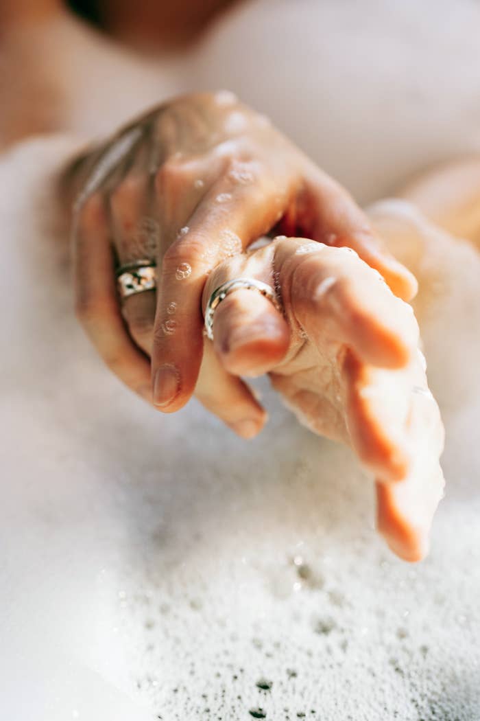 Hands intertwined successful  a bubble bath, adorned with rings, emphasizing relaxation and luxury