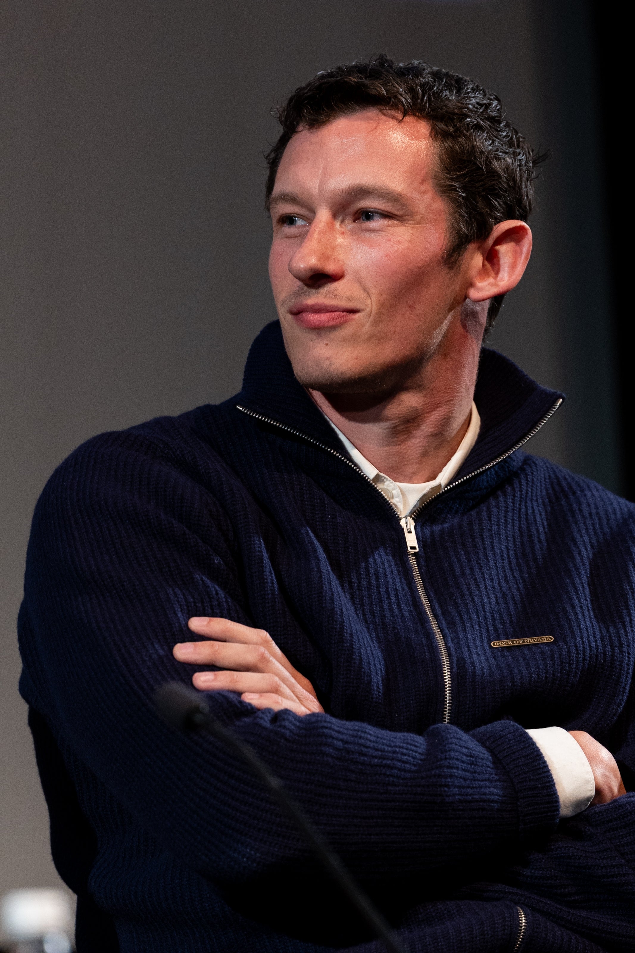 Person successful a ribbed zip-up sweater with arms crossed, gazing sideways thoughtfully successful a casual setting