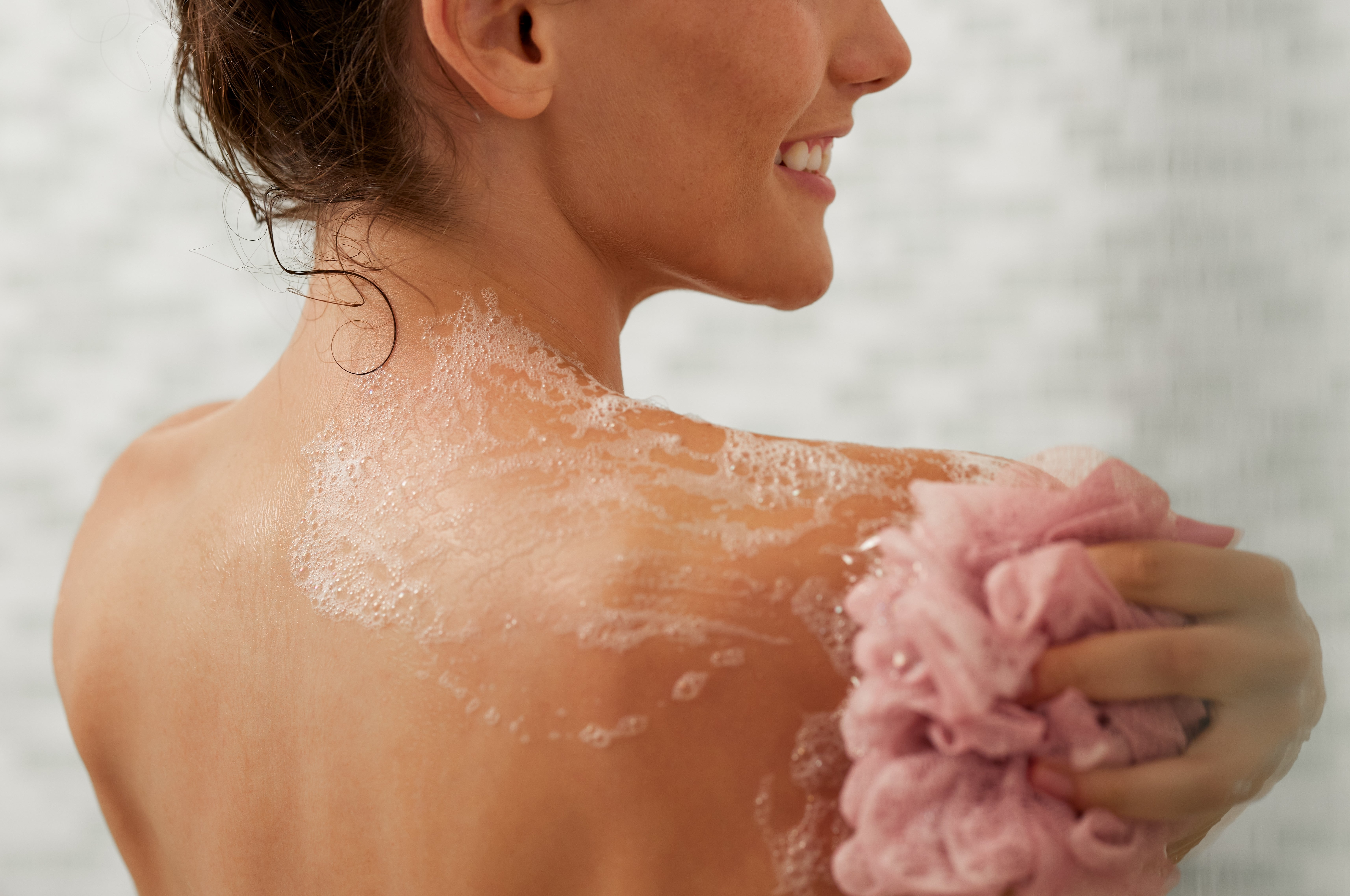 Person smiling portion applying assemblage lavation with a loofah connected their enarthrosis successful the shower