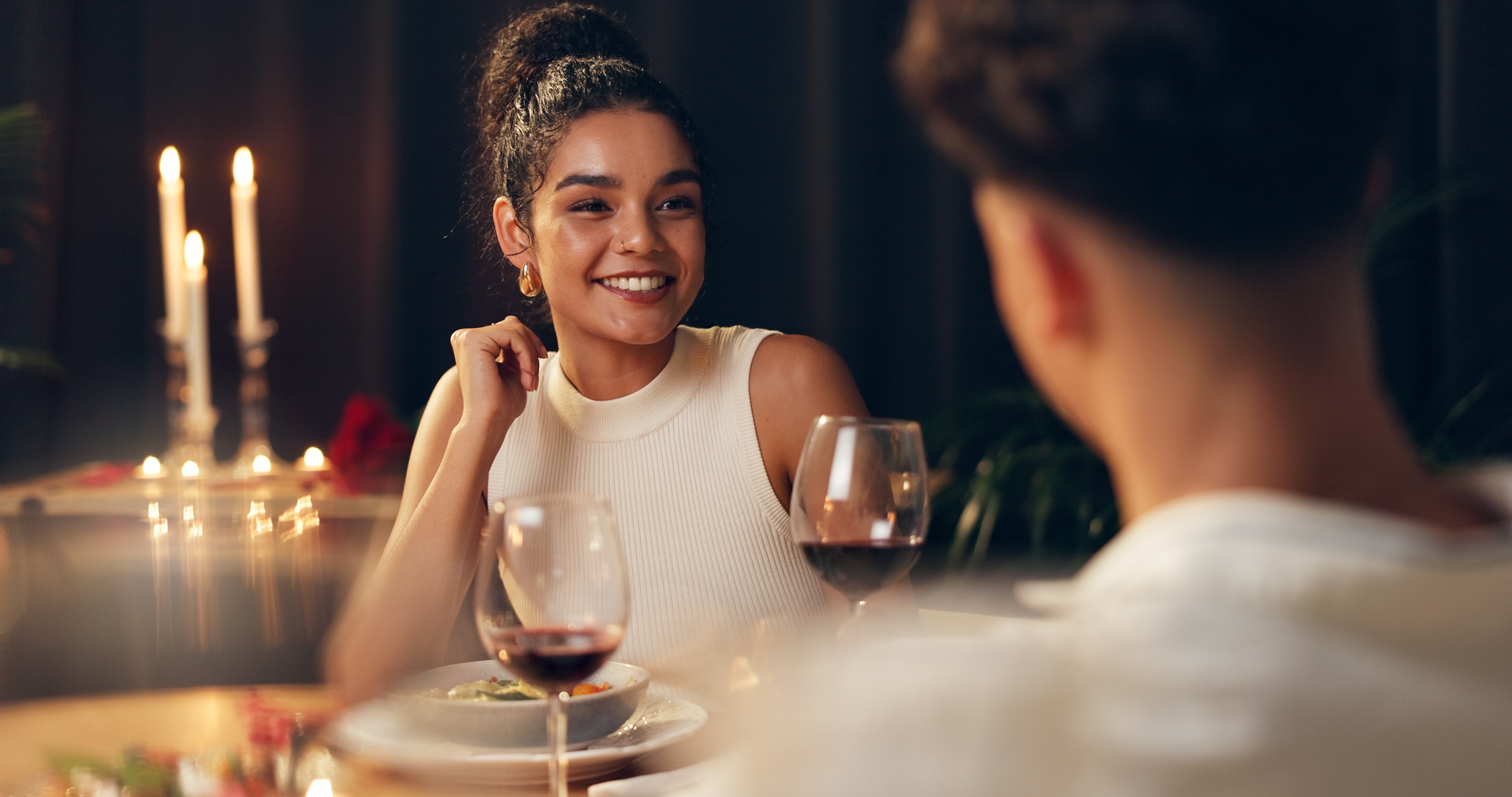A mates enjoys a romanticist candlelit dinner, smiling astatine each different crossed the array with glasses of vino and cozy ambiance