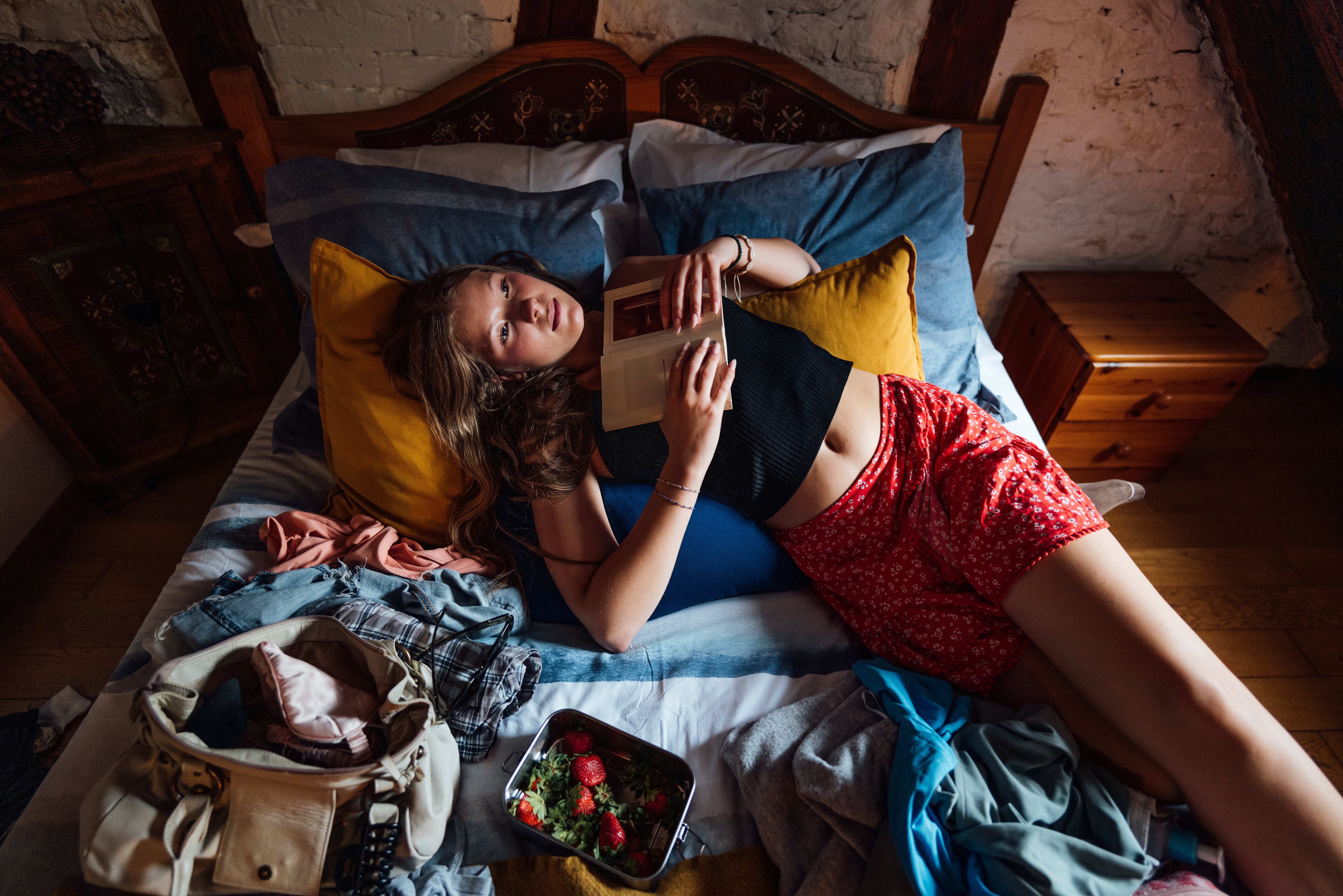 Person lying connected furniture with a book, wearing a sleeveless apical and patterned shorts. A container and a nutrient instrumentality are connected the bed