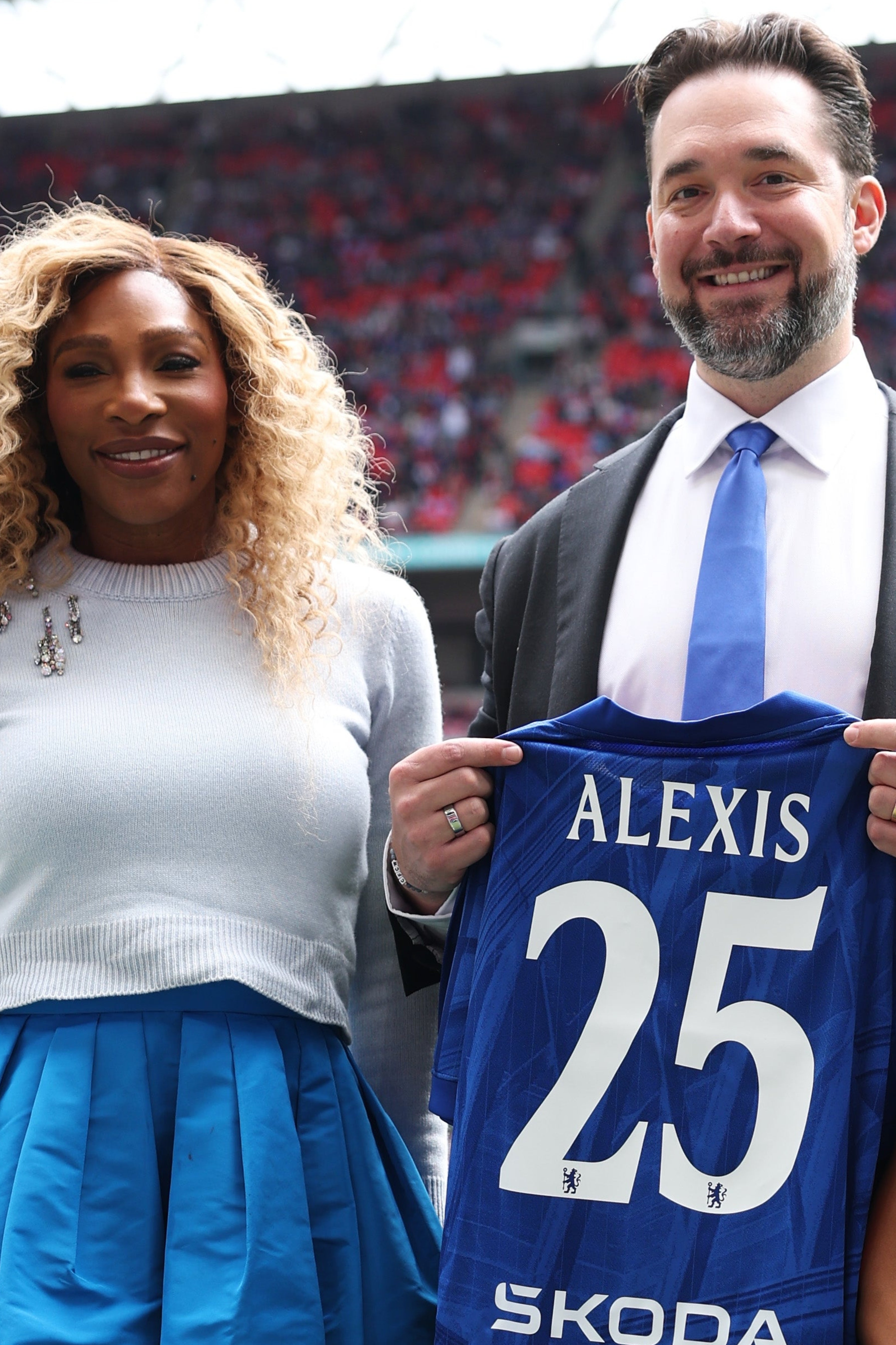 Three radical   lasting  connected  a sports field, holding a customized  jersey with "Alexis 25." The pistillate   wears a stylish blouse and skirt ensemble