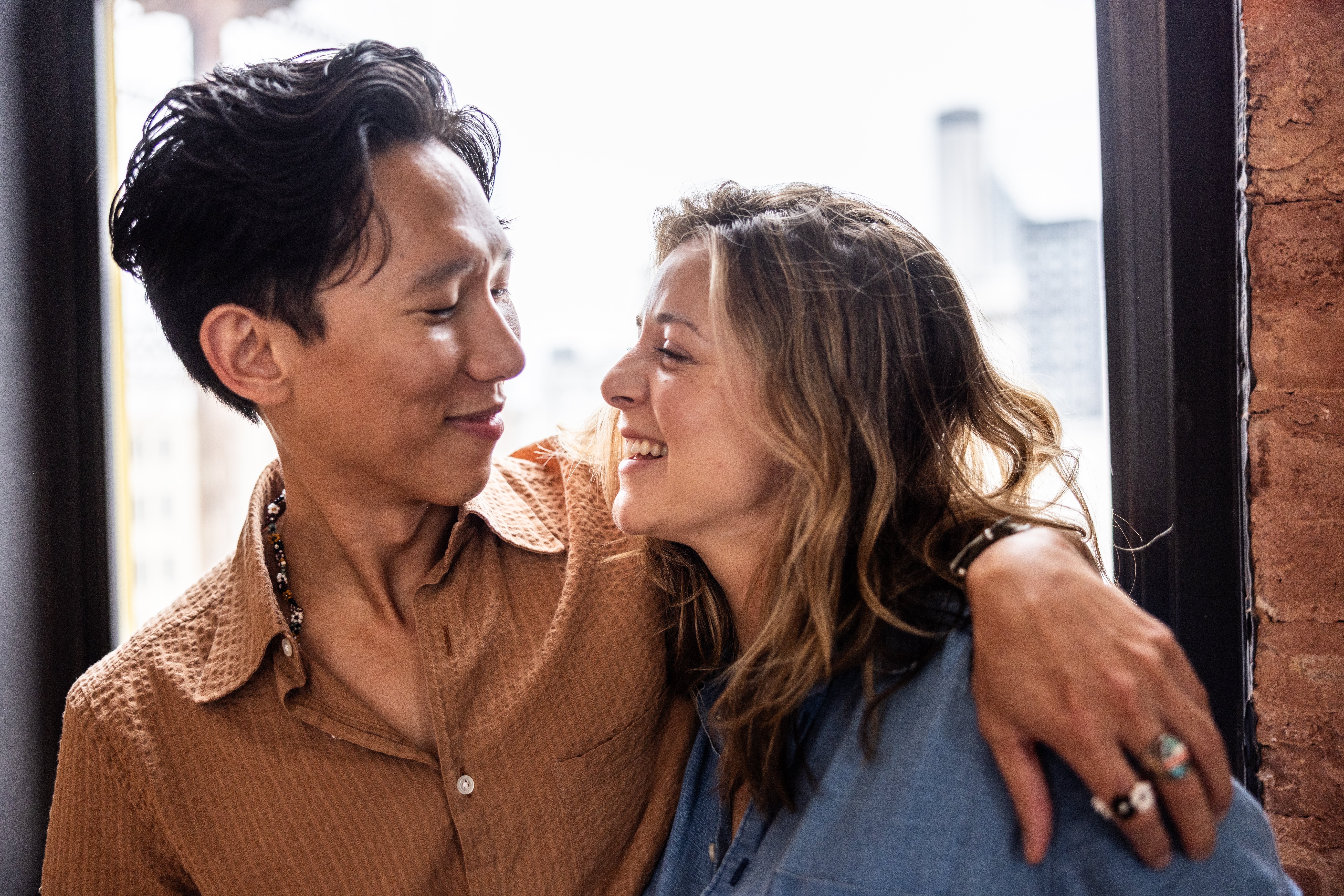 A mates shares a tender moment, smiling astatine each different affectionately portion embracing by a window