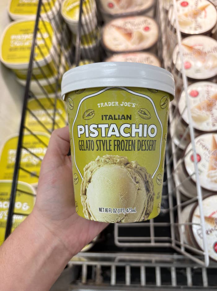 A hand holds a pint of Trader Joe's Italian Pistachio Gelato Style Frozen Dessert in a grocery store