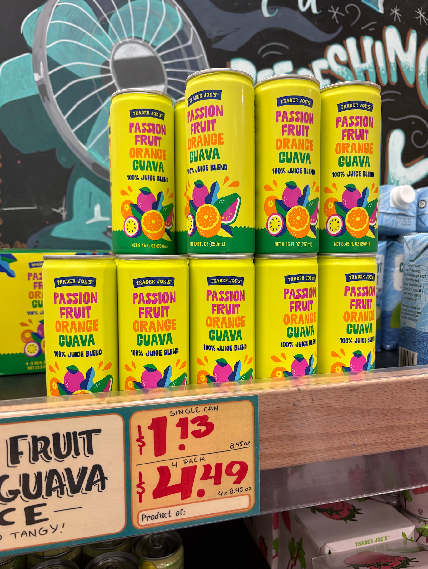 Cans of Trader Joe's Passion Fruit Orange Guava juice displayed on a shelf, with price tags showing $1.49 for a single can and $4.49 for a 4-pack