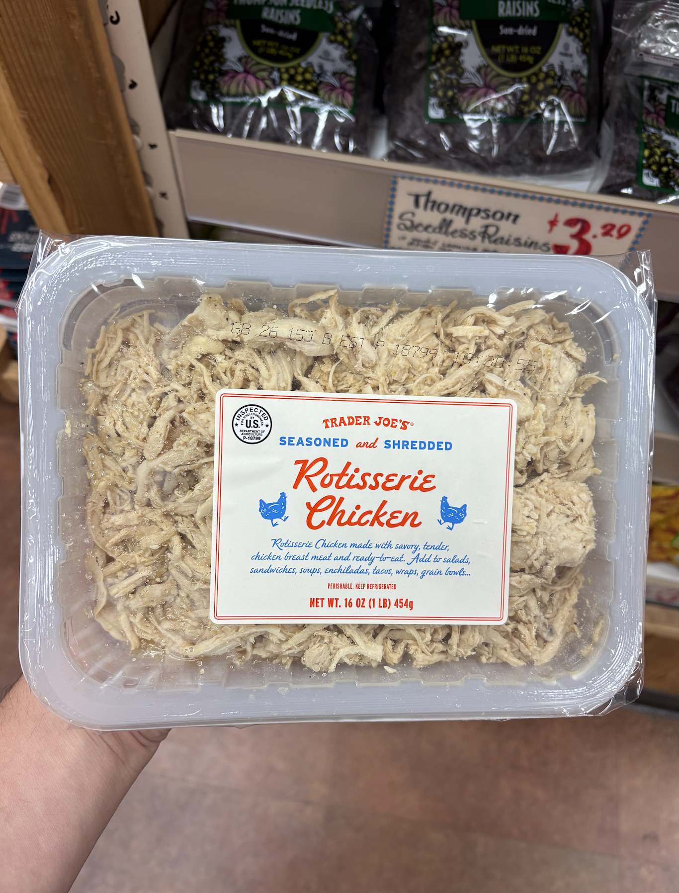 Package of Trader Joe's seasoned and shredded rotisserie chicken held in a hand, displayed in-store