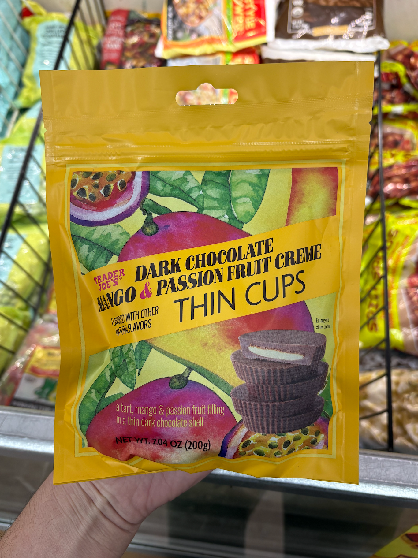 Package of Trader Joe's Dark Chocolate Mango &amp;amp; Passion Fruit Creme Thin Cups held in front of a freezer section