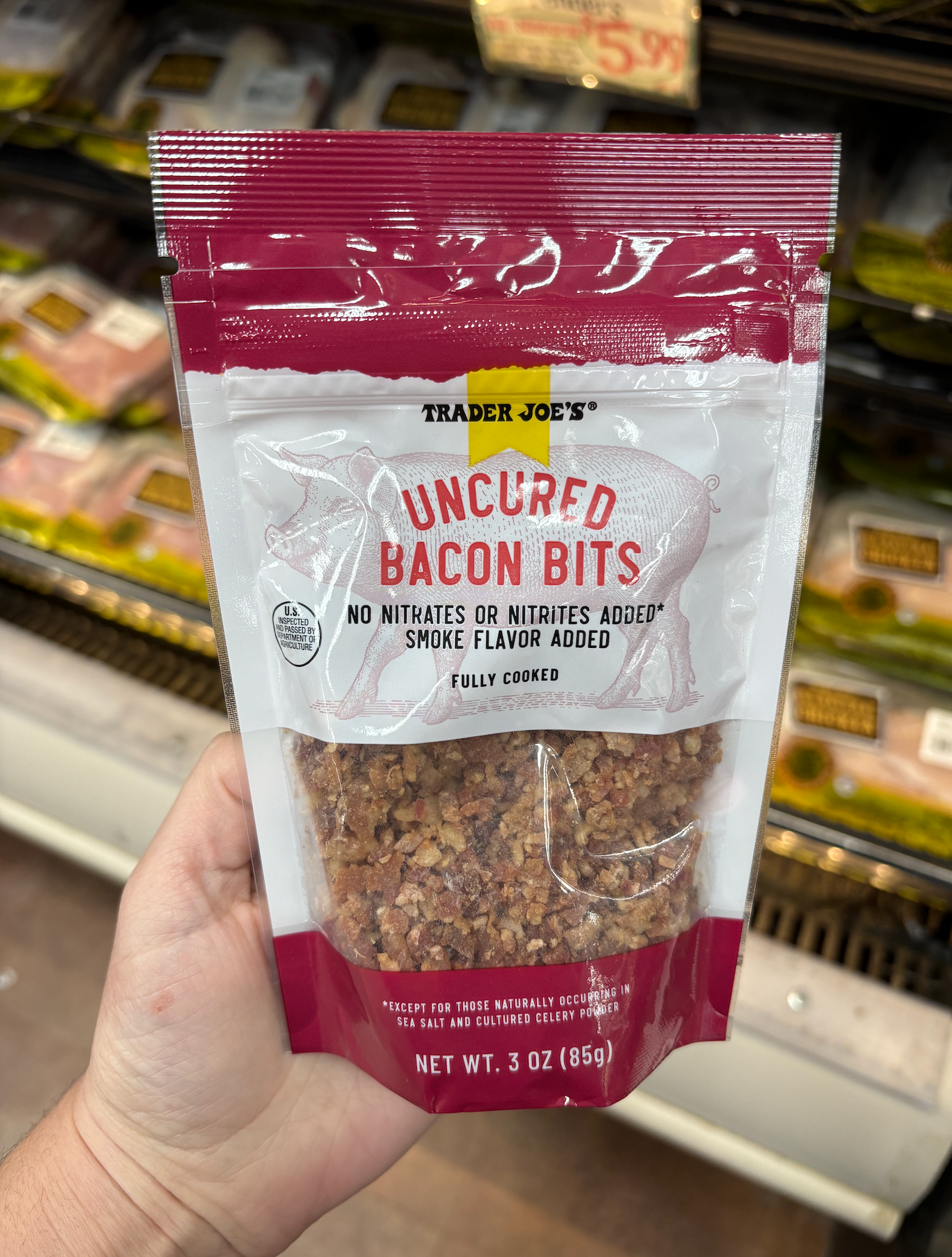 Hand holding a package of Trader Joe's uncured bacon bits, labeled as fully cooked with no nitrates or nitrites added