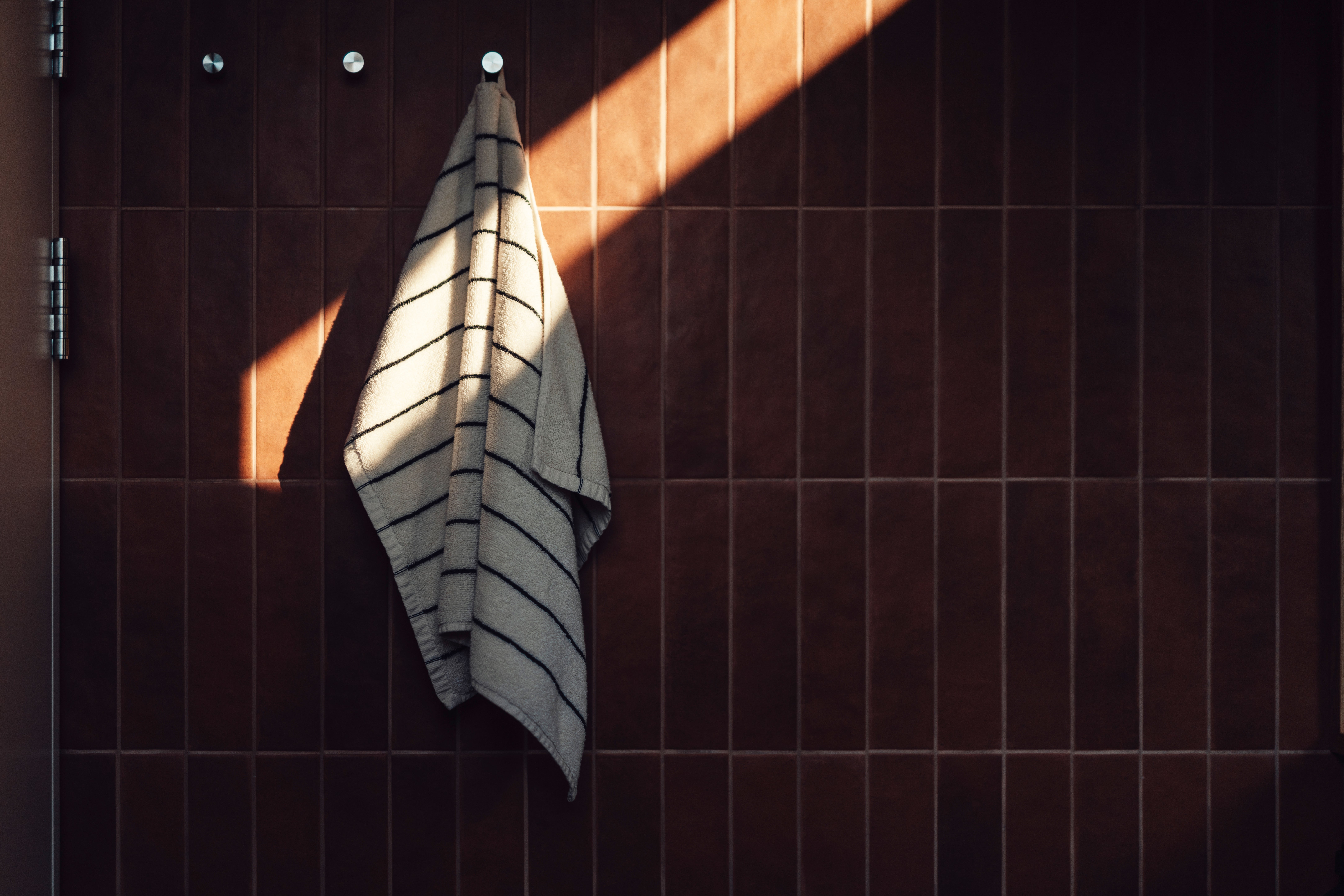A towel with stripes hangs connected a partition with sunlight streaming in, creating a peaceful atmosphere