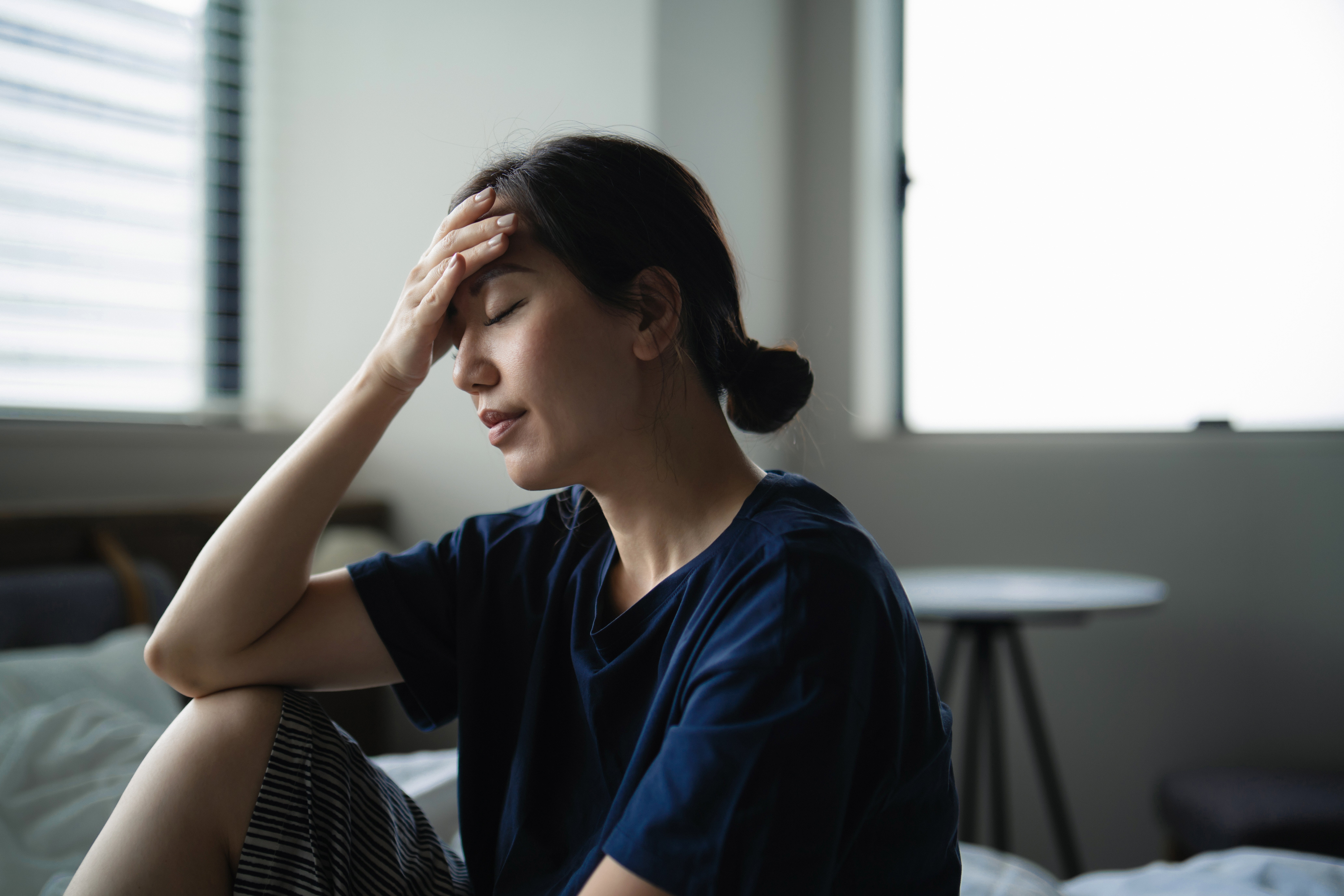 Person sitting indoors, holding caput  with a hand, looking fatigued oregon  stressed, suggesting a imaginable  wellness  contented   specified  arsenic  headache oregon  fatigue