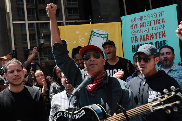 A instrumentalist  holds a guitar and raises a fist successful  beforehand   of a assemblage  astatine  a protest. Banners with multilingual substance   are disposable   successful  the background