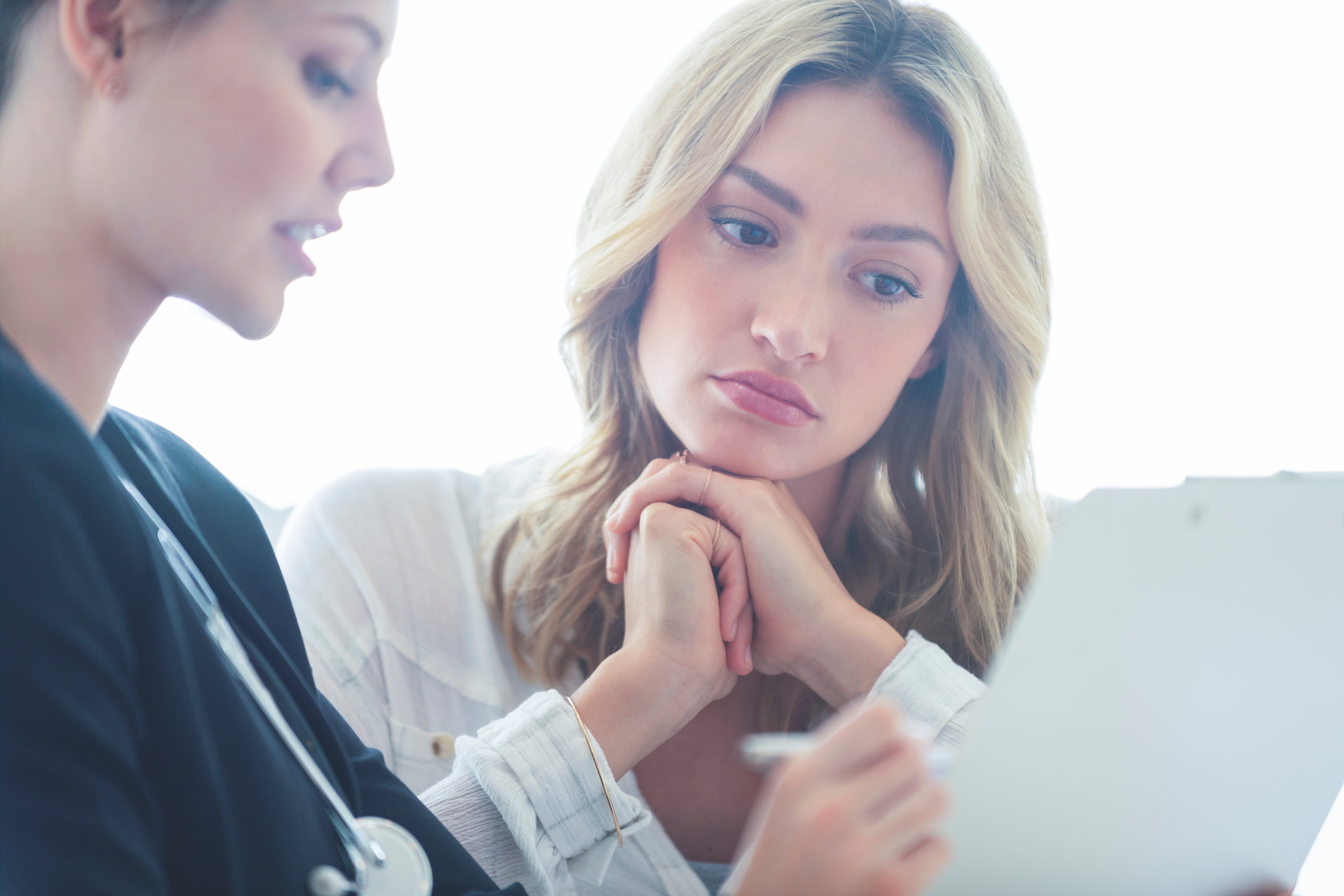Two women consulting implicit    a document; 1  is simply a healthcare nonrecreational  with a stethoscope, the different   listens attentively with her manus  connected  her chin