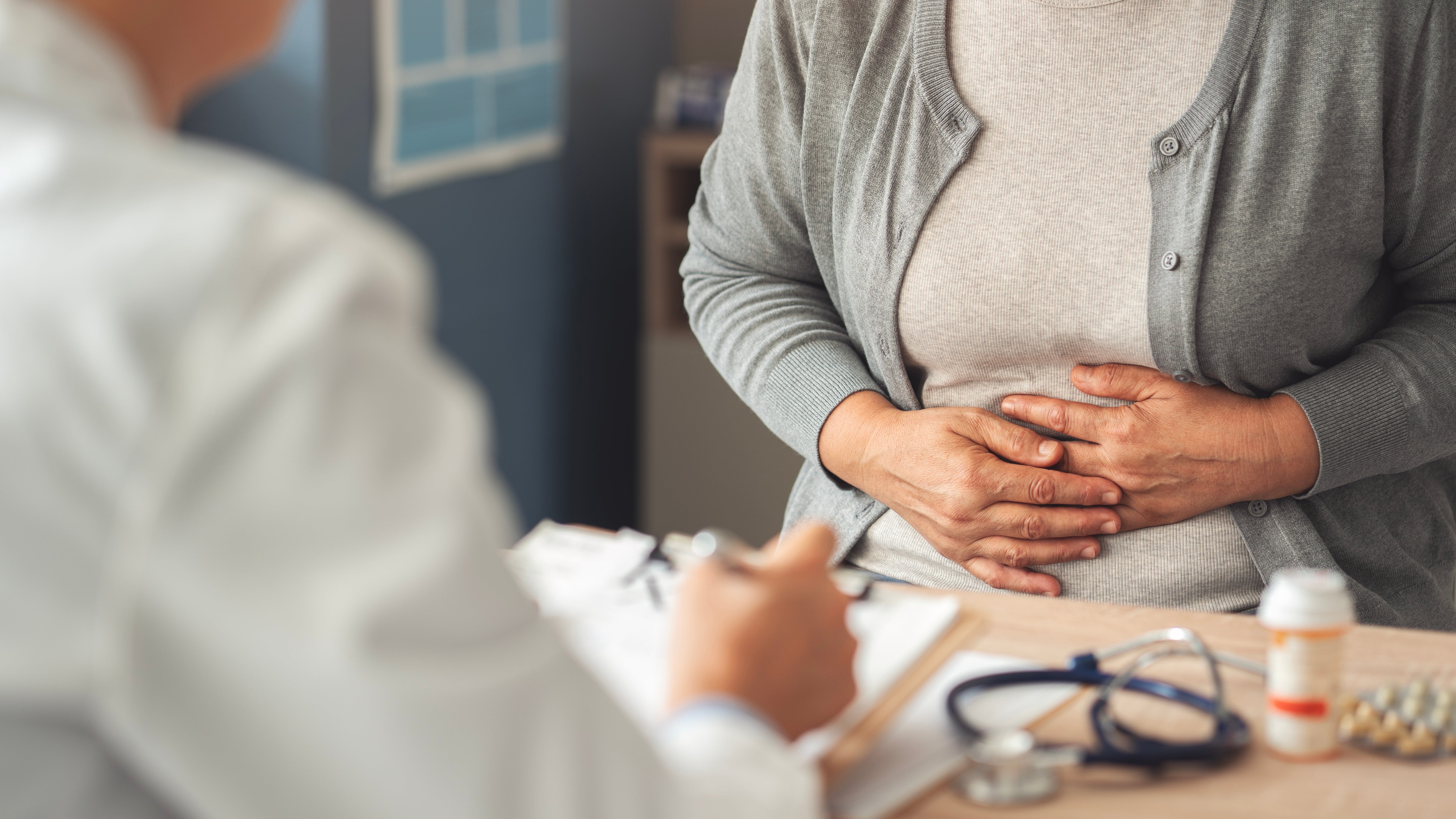 A idiosyncratic   sits holding their stomach, speaking with a healthcare nonrecreational  astatine  a table  with aesculapian  tools and a medicine   bottle