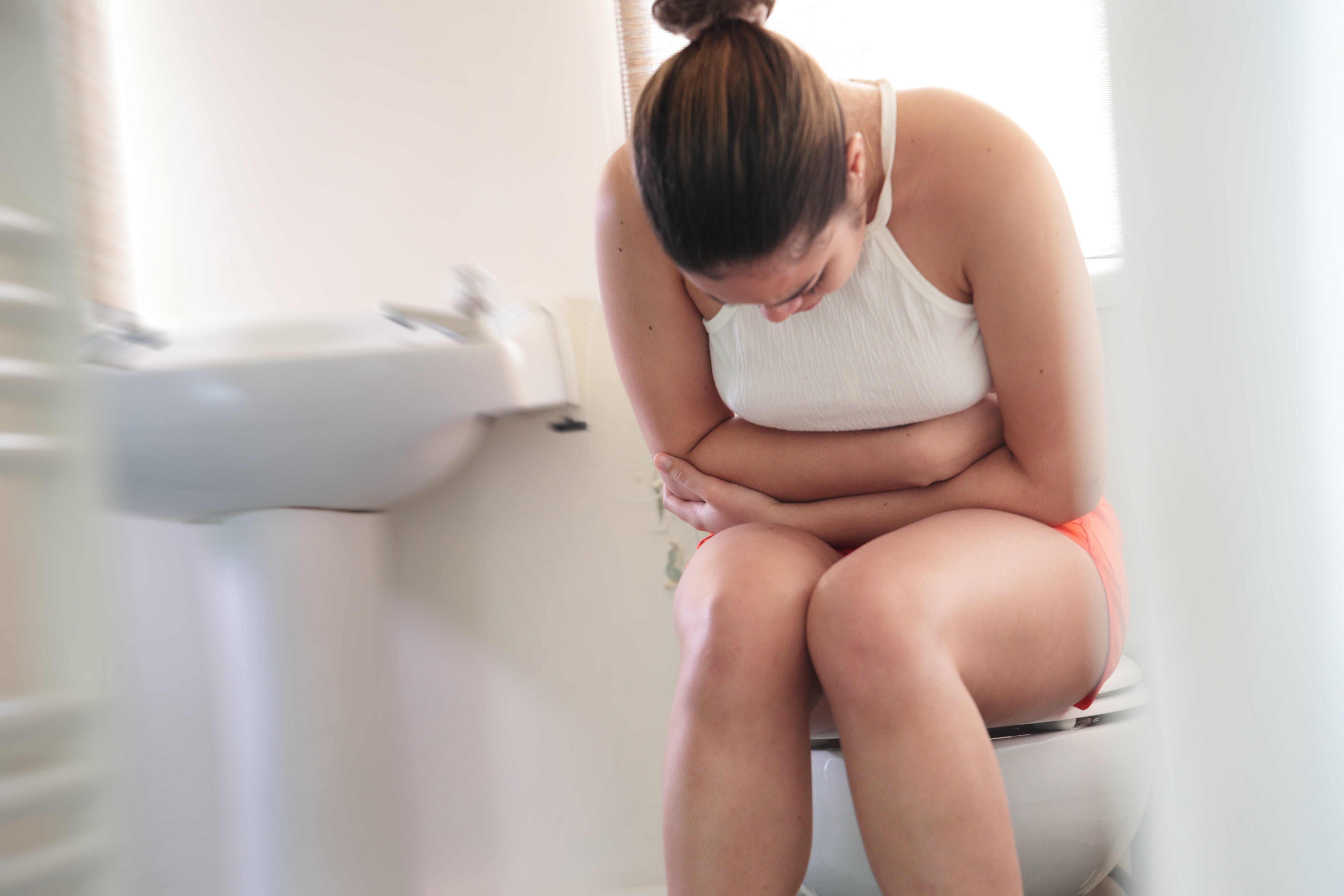 Person sitting connected  a toilet holding their stomach, appearing to beryllium  successful  discomfort, conveying a health-related issue