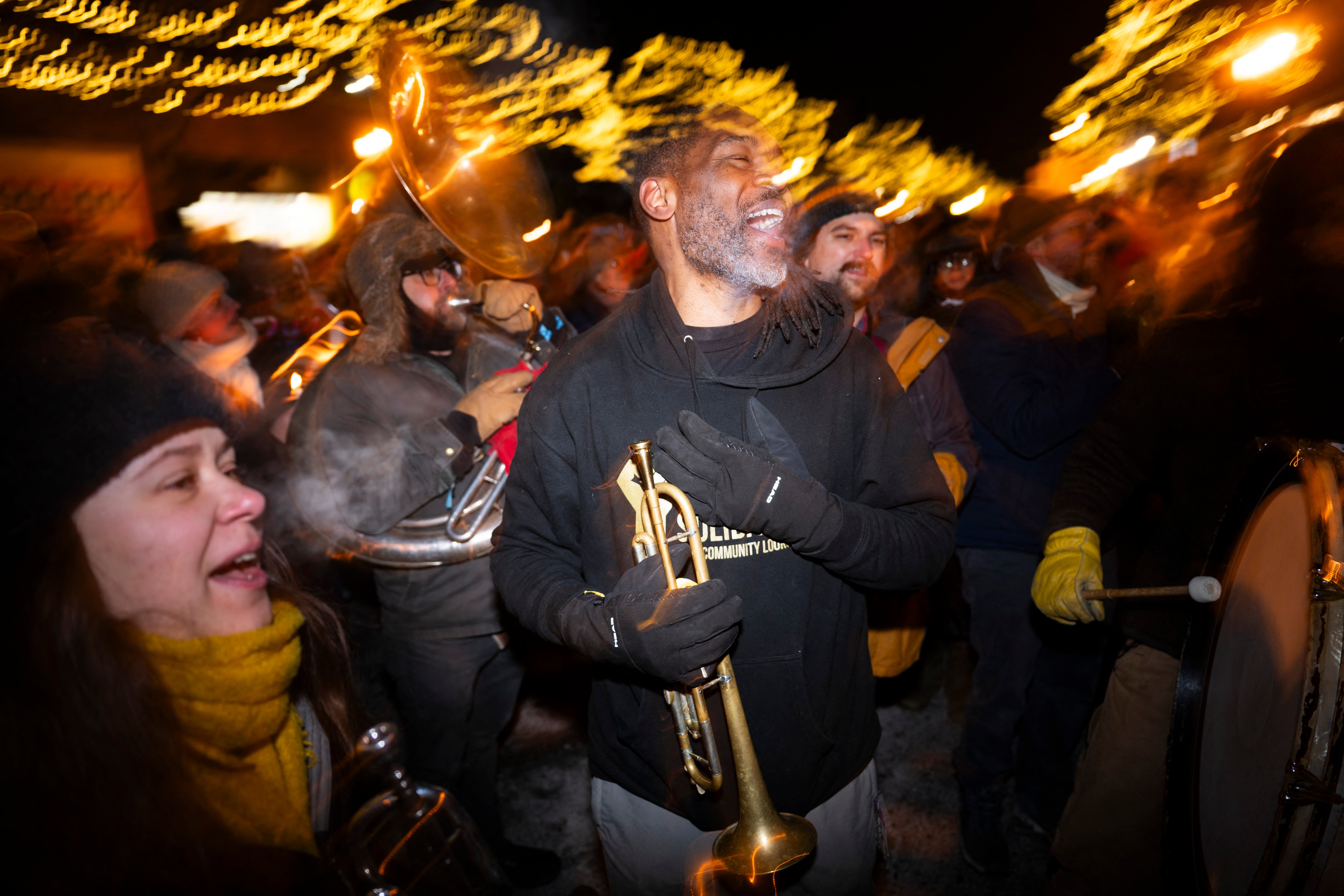 A joyful brass set performs outdoors astatine night, surrounded by a festive assemblage nether glowing lights