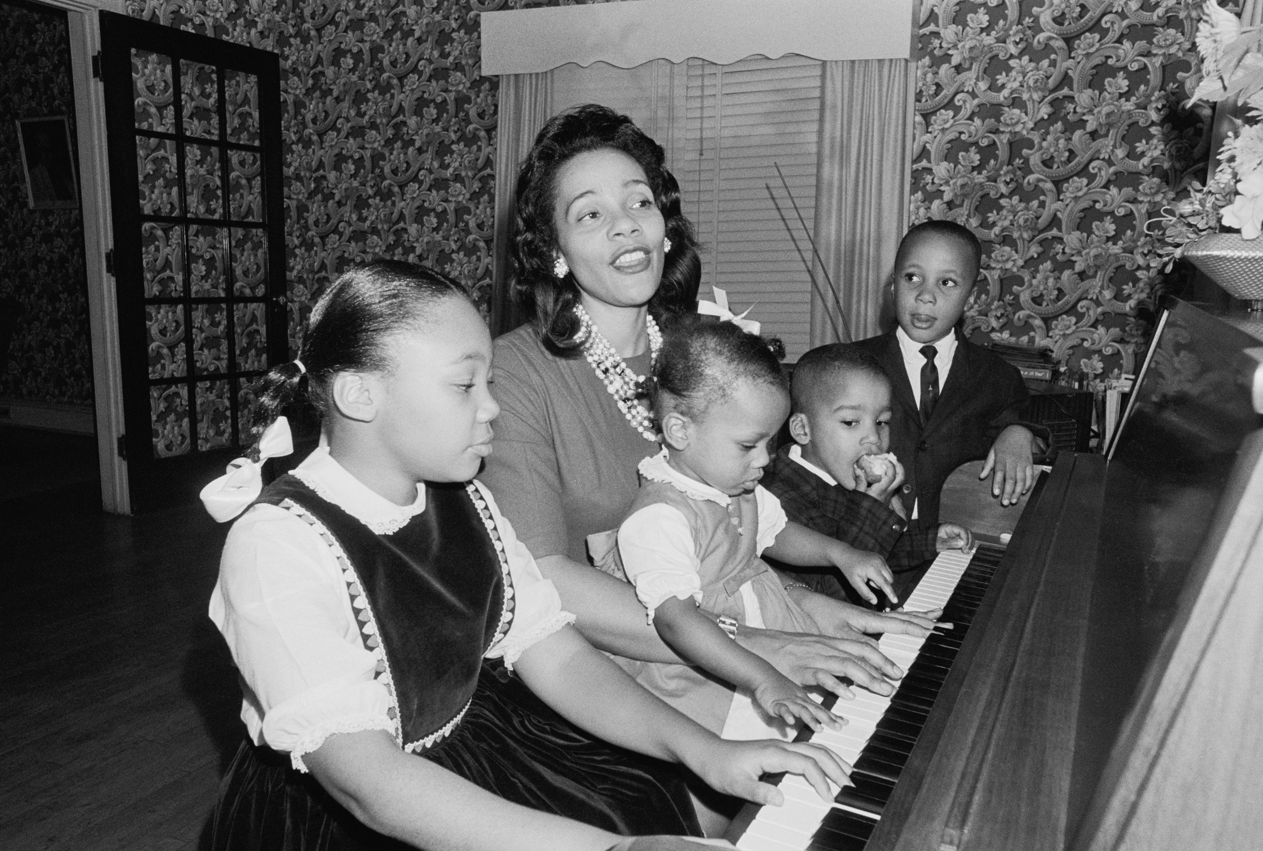 A pistillate and 4 children stitchery astir a piano, with the older kid playing. The pistillate and children look to beryllium enjoying the infinitesimal together