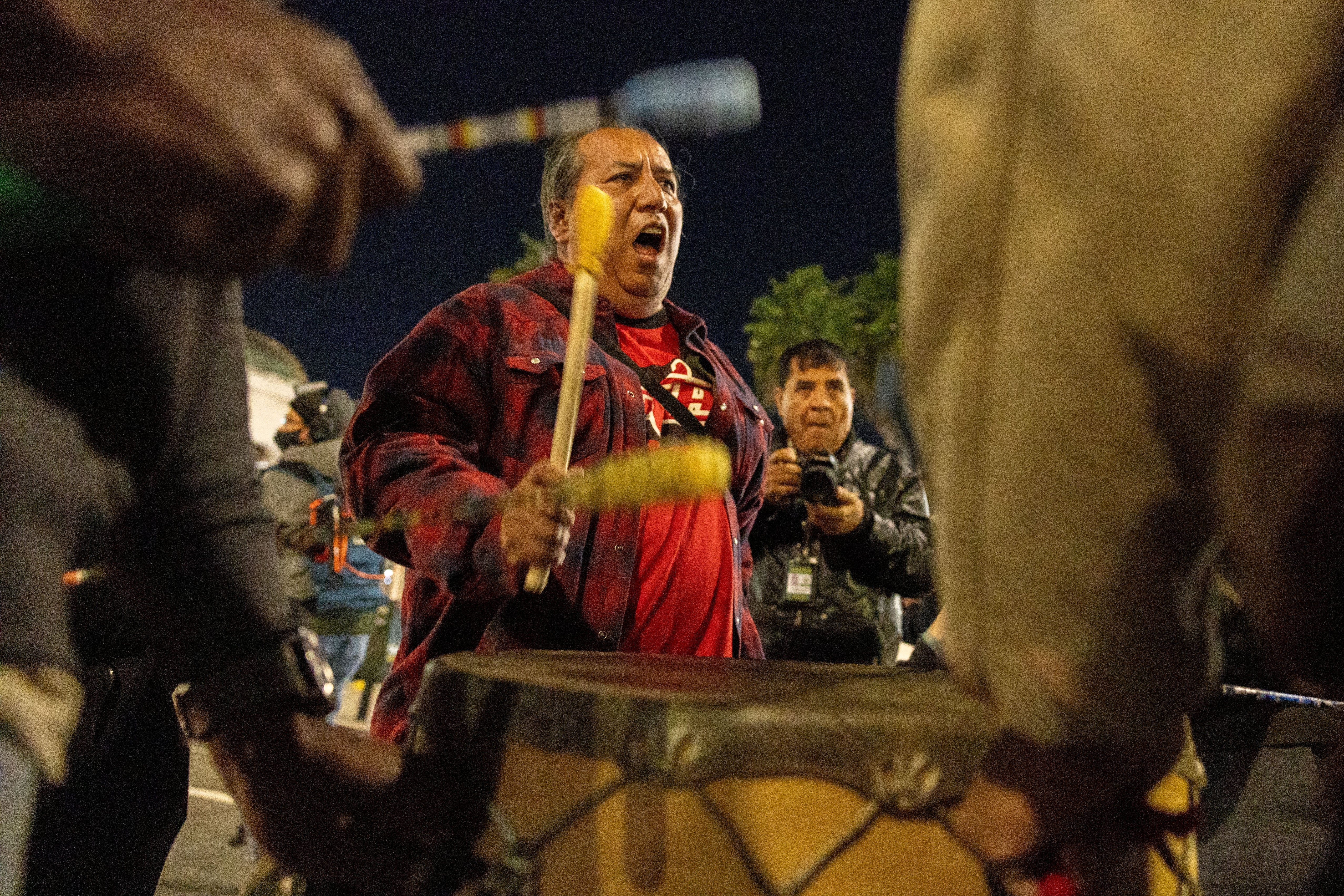 A antheral passionately plays a ample drum during a nighttime gathering, surrounded by others with drums
