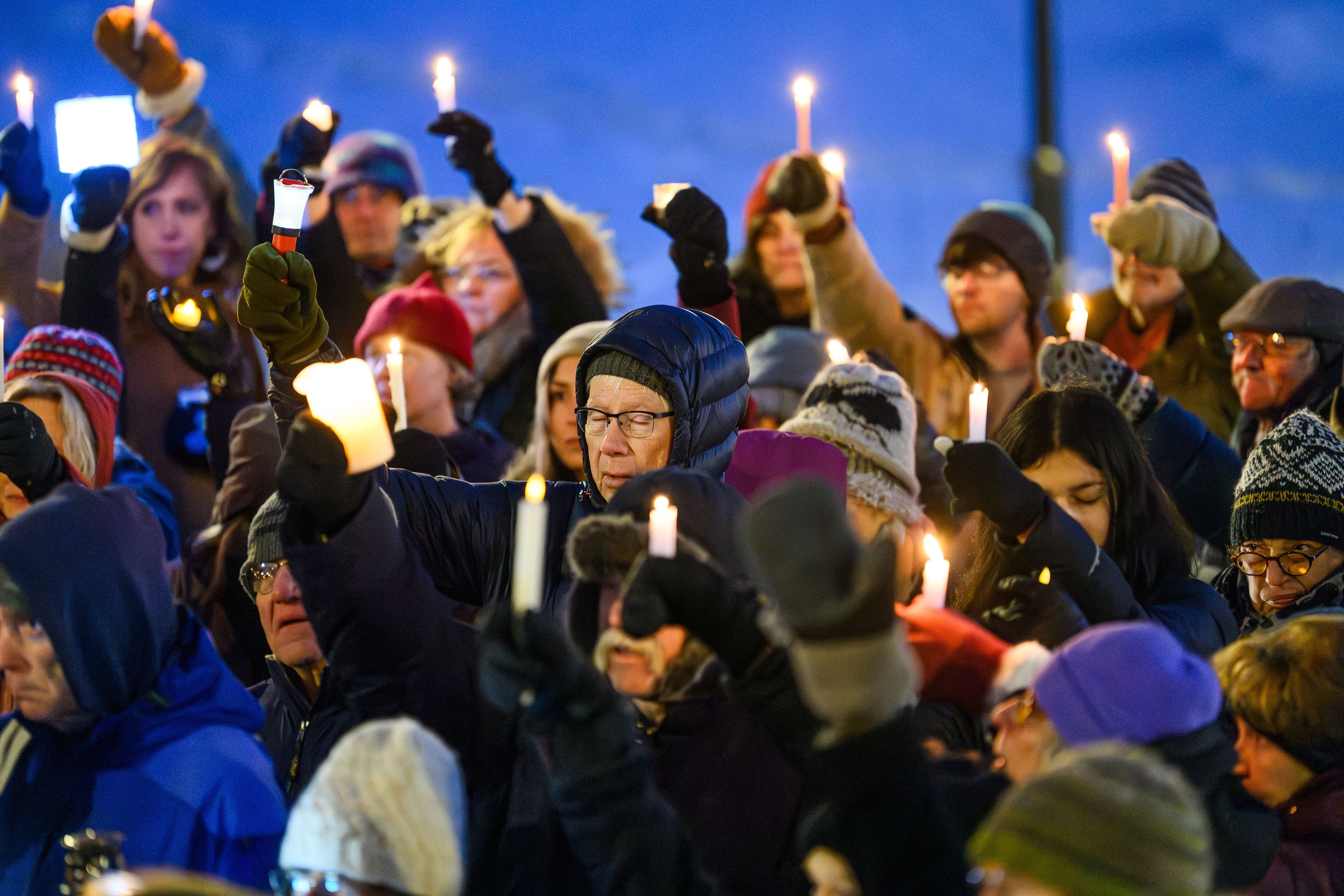 A radical of radical holding candles during a vigil, solemn expressions, dressed warmly for acold weather