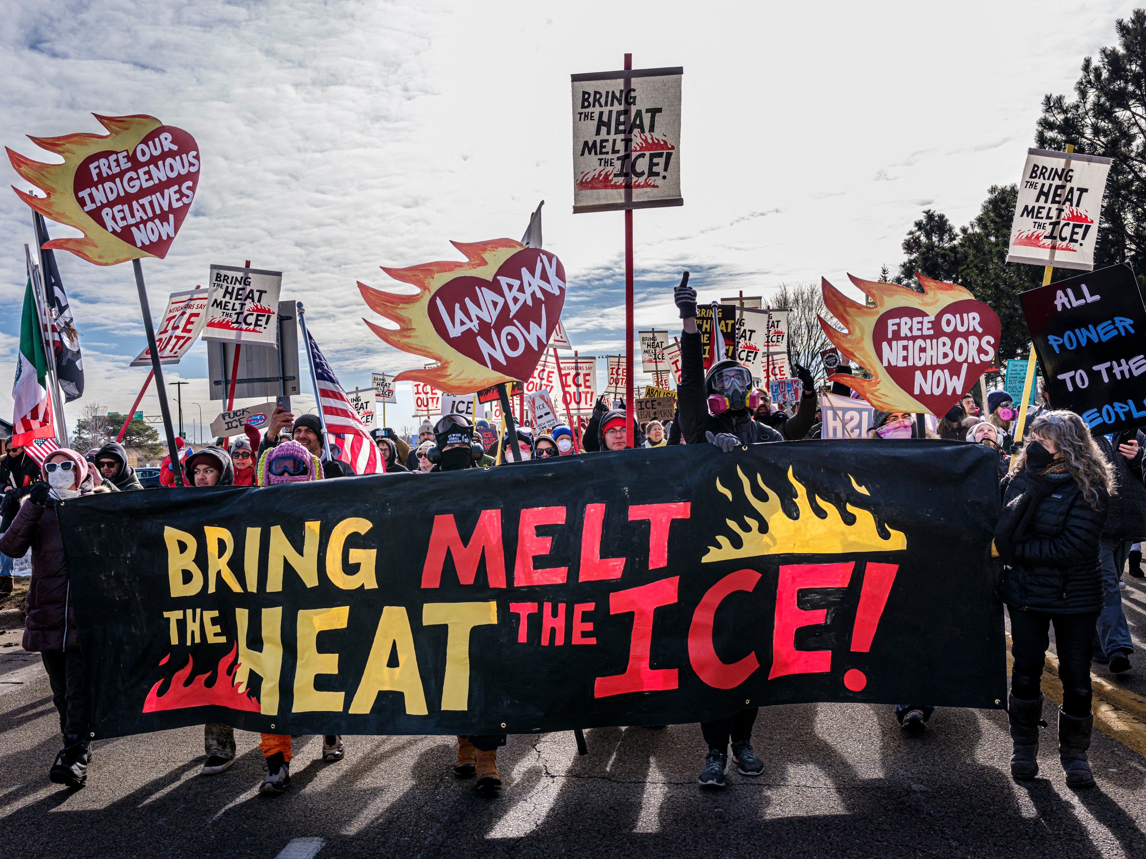 Protesters march holding signs demanding migration betterment and clime action, including "Melt the ICE" and "Free Our Neighbors" banners