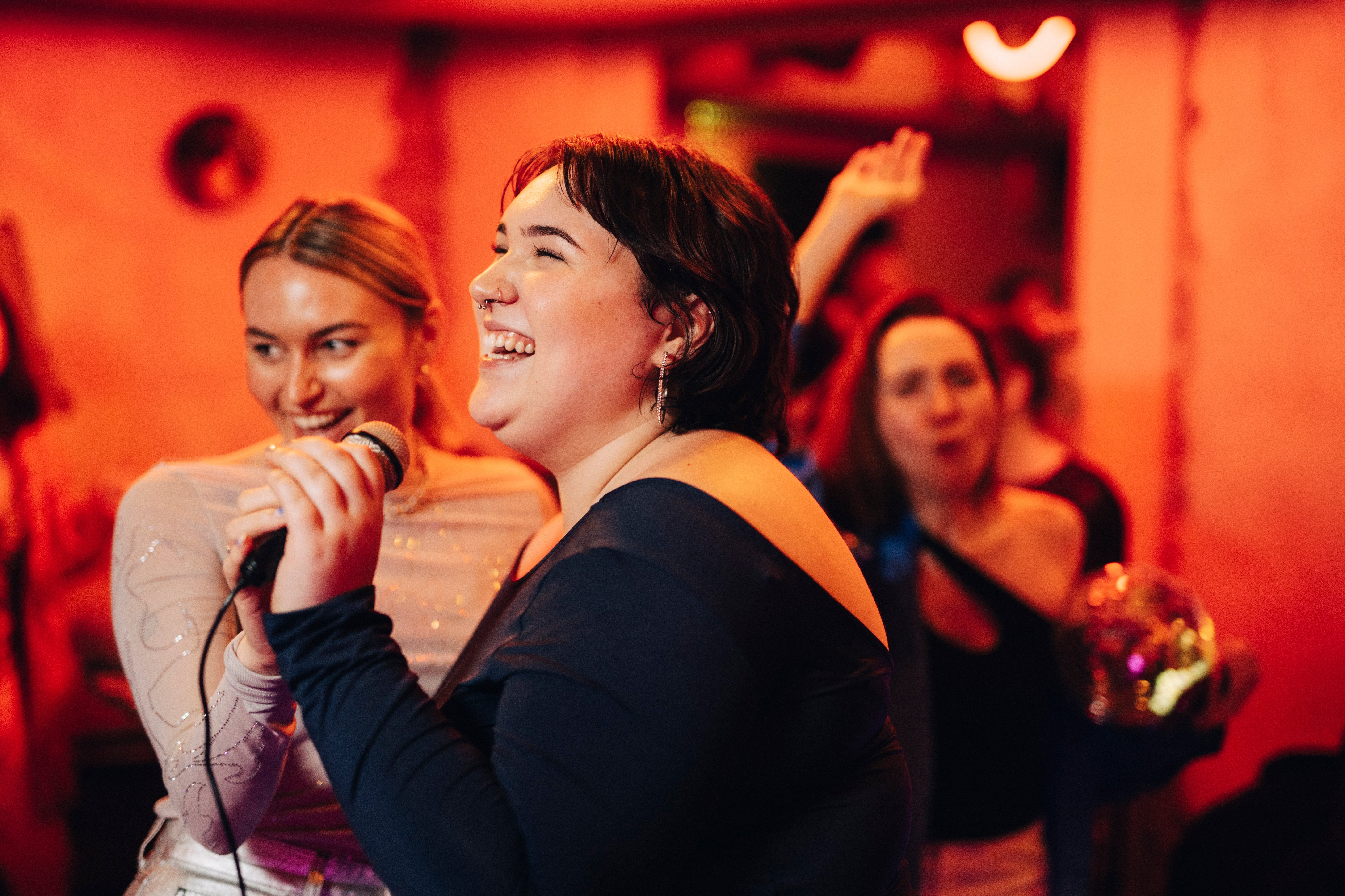 Two radical joyfully singing into a microphone astatine a lively event, with others celebrating successful the background