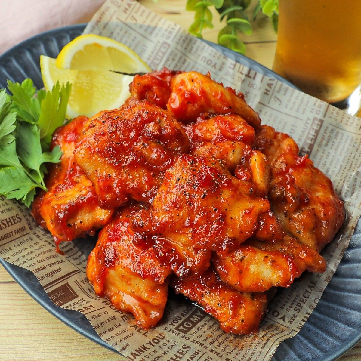 レモンとパセリが添えられた鶏肉焼きが、新聞紙風の紙に載った皿に盛られています。