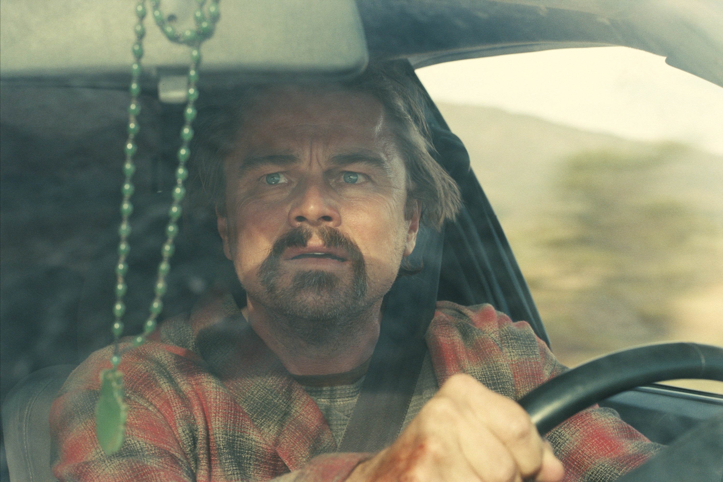 Leonardo DiCaprio driving in the movie One Battle After Another looking distraught