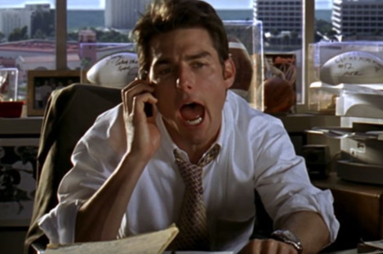 A person in an office, mid-conversation on the phone, appears animated and emphatic with their expression and open mouth