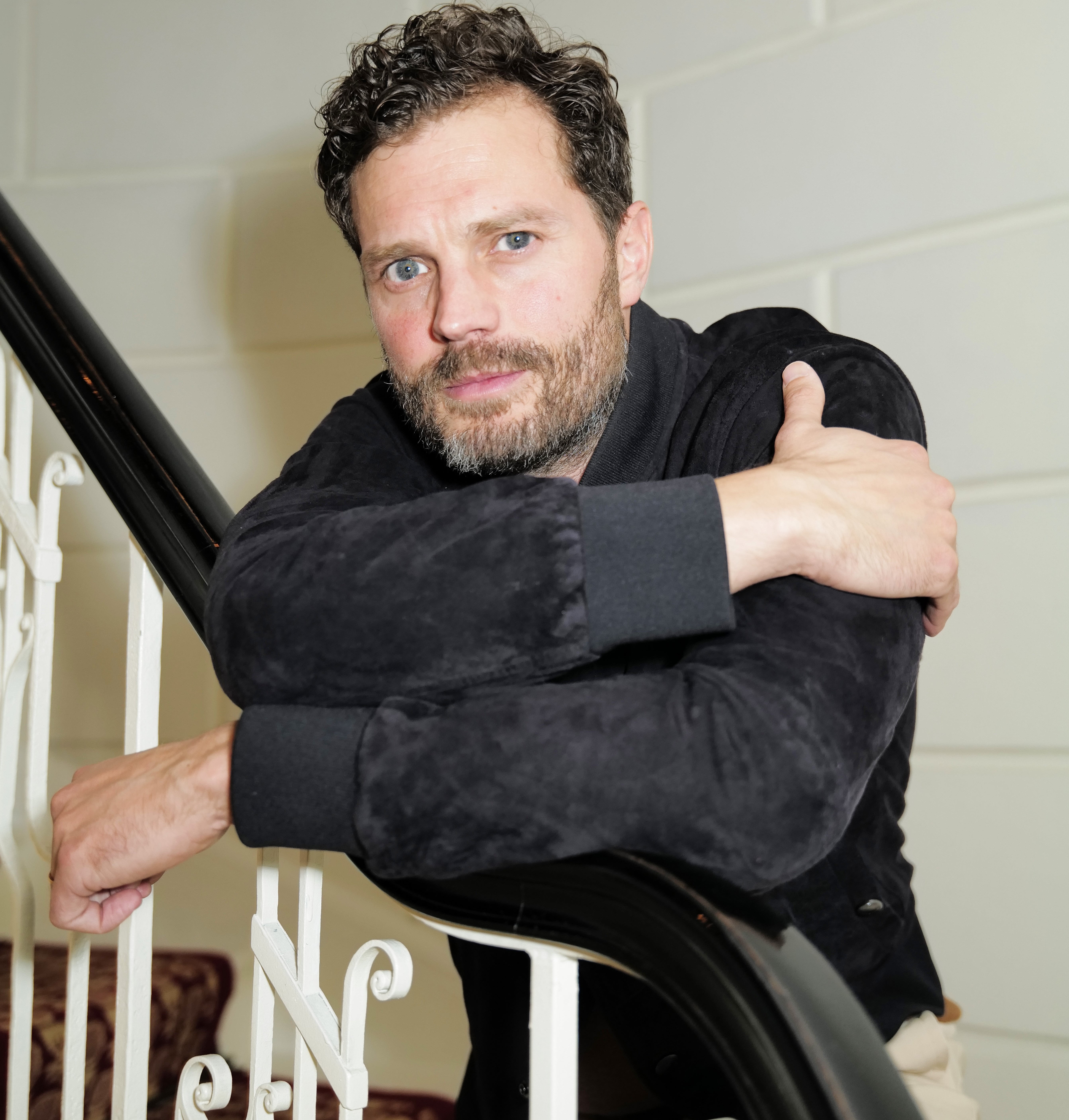 Jamie Dornan leaning on a staircase railing looking directly at the camera