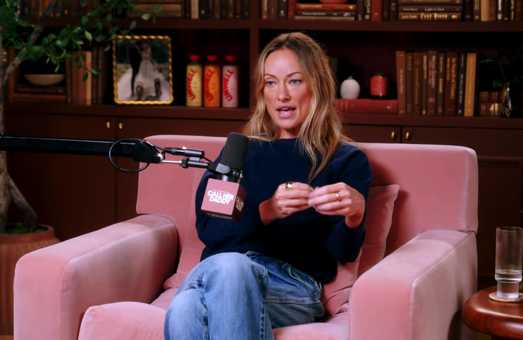 Person successful  a relaxed setting, speaking connected  a podcast. Seated successful  a pinkish  chair, wearing a casual long-sleeve apical  and jeans. Microphone nearby