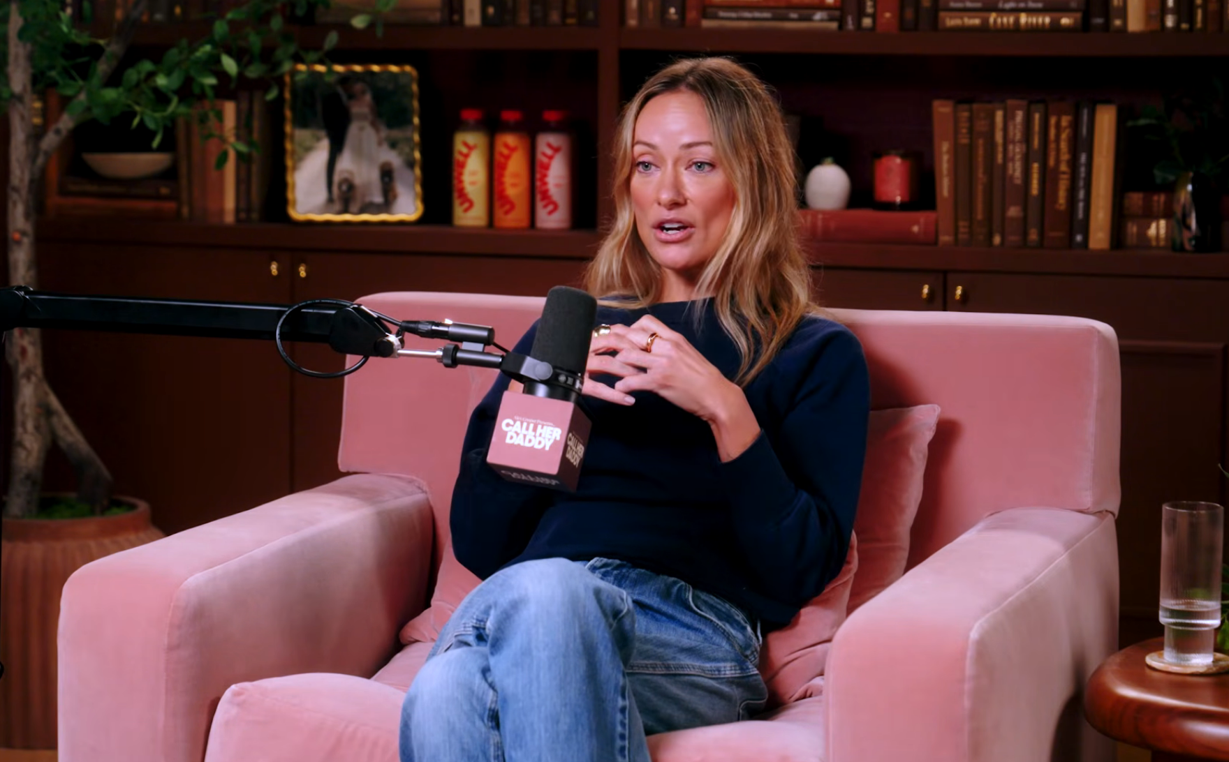 Person sitting successful  a studio, speaking into a microphone during a podcast recording, with bookshelves successful  the background