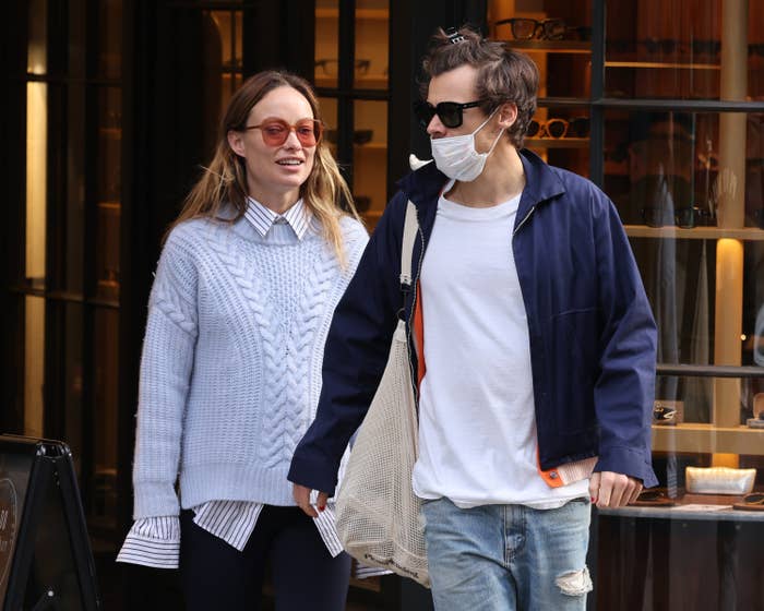 Two radical   walking together, 1  successful  a striped garment  nether  a cable-knit sweater, the different   successful  sunglasses, a jacket, and jeans, wearing a mask