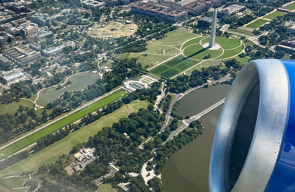 View of the Washington Monument from an airplane window, surrounded by greenish parks and adjacent buildings
