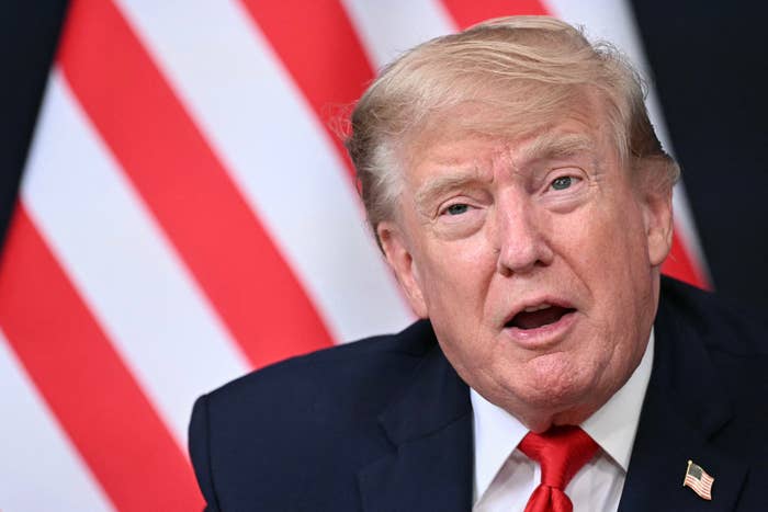 A idiosyncratic   successful  a suit   and reddish  necktie  speaks successful  beforehand   of a backdrop with reddish  and achromatic  stripes