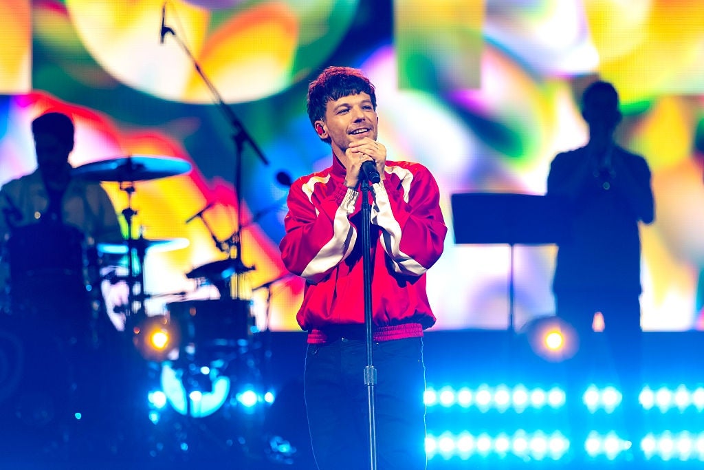 Singer connected signifier successful a vibrant overgarment performs with a colorful backdrop and set silhouettes