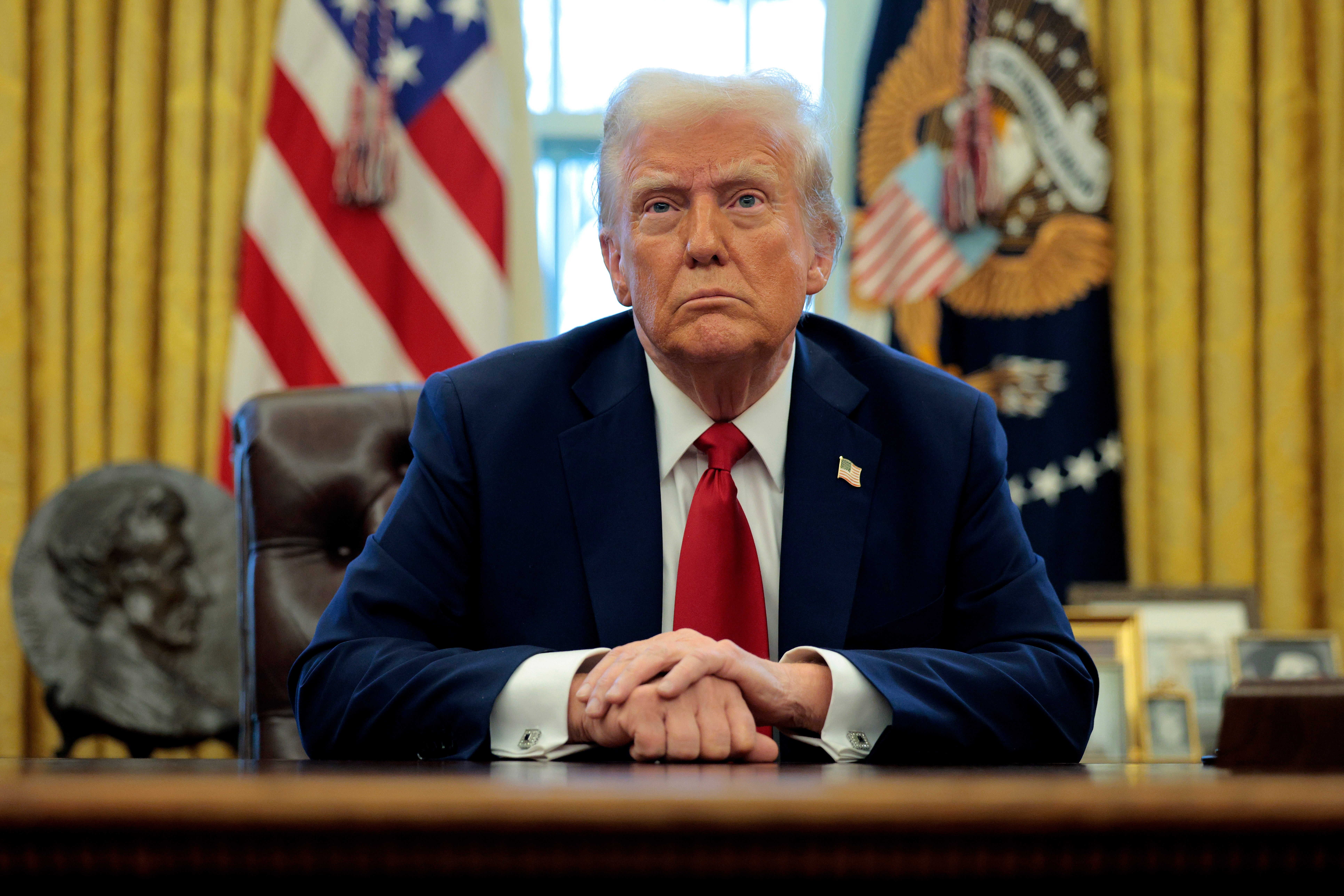 A idiosyncratic successful a suit sits astatine a table successful an authoritative country with U.S. flags and a salient seal successful the background