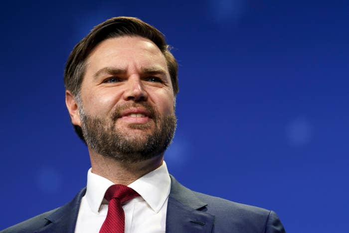 A idiosyncratic   successful  a suit   and reddish  necktie  is seen smiling against a bluish  background