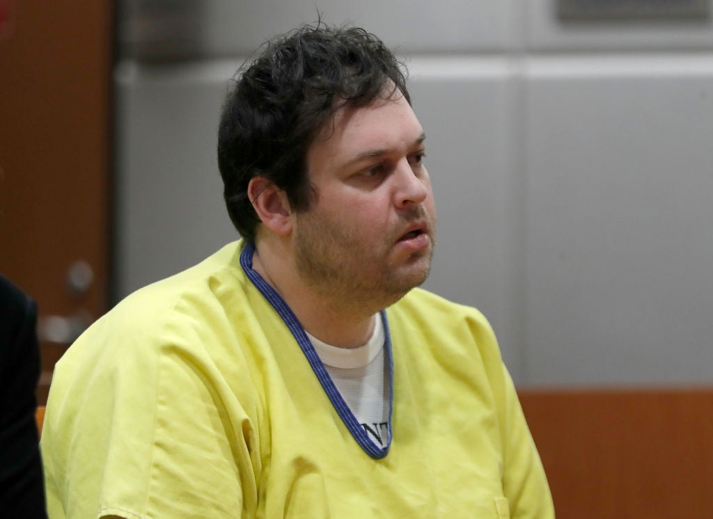 A man in a courtroom setting wears a yellow prison uniform, appearing attentive during proceedings